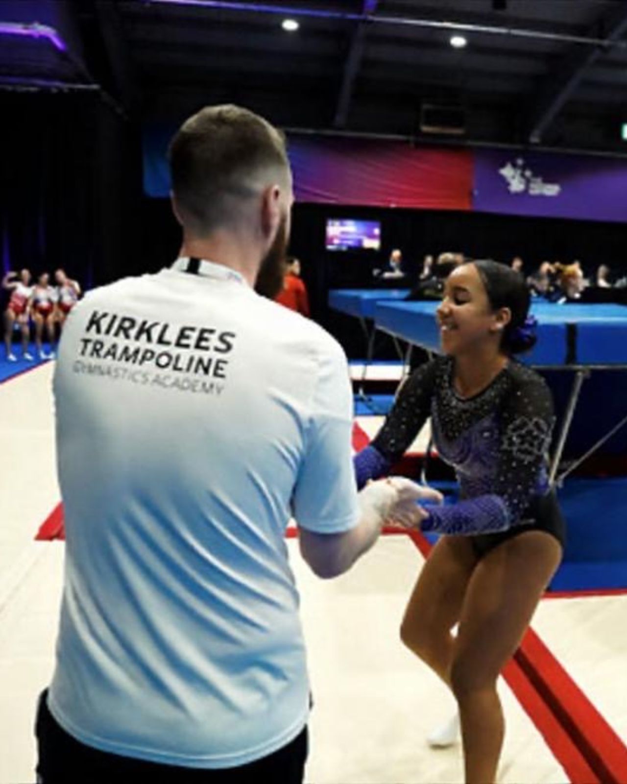 A KTGA coach supporting a gymnast during a trampoline class