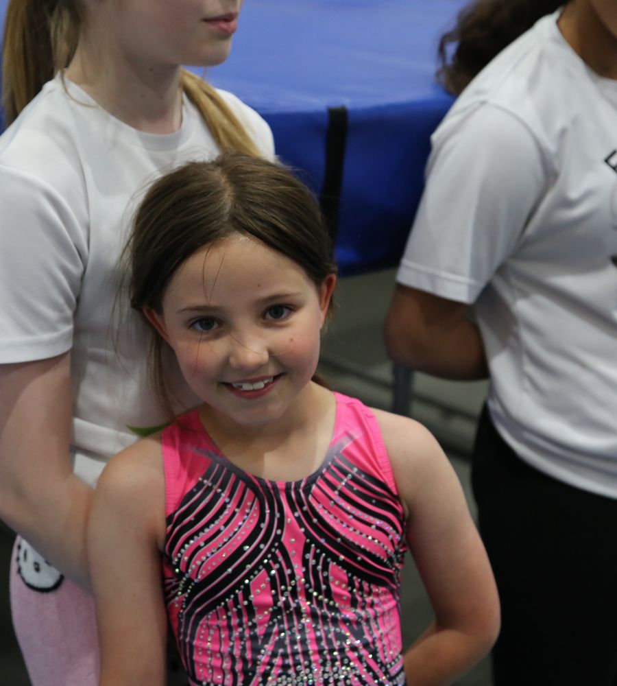 A smiling gymnast in a pink leotard at the academy