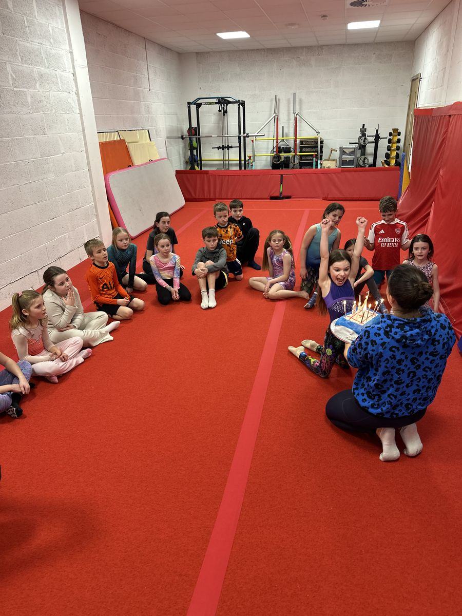Children and coaches sitting together in a circle on the gym floor, with a birthday cake