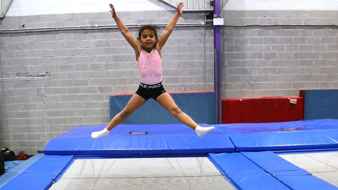 A young gymnast doing a star jump on a trampoline